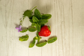 Fresh strawberries and peppermint leaves arranged on a wooden table.