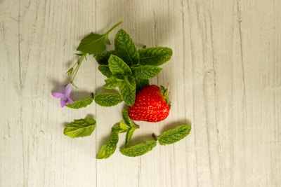 Fresh strawberries and peppermint leaves arranged on a wooden table.