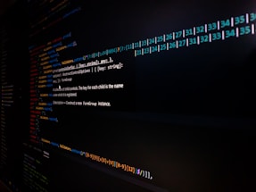 Lines of code are displayed on a computer screen, featuring syntax highlighting with different colors to distinguish functions, variables, and annotations. The image is somewhat dark, focusing on the brightly colored text on a black background.