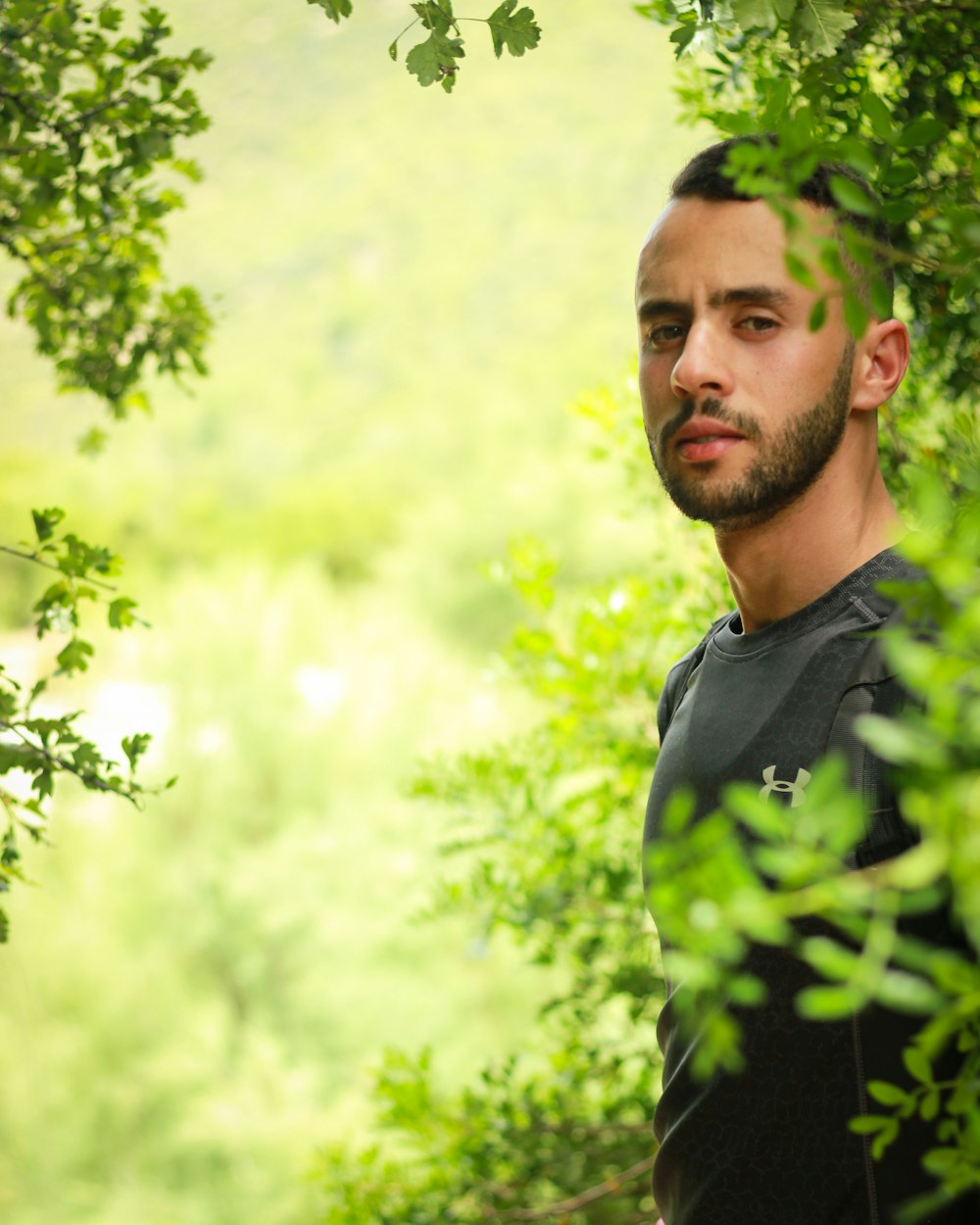 man in black and green polo shirt standing near green tree during daytime