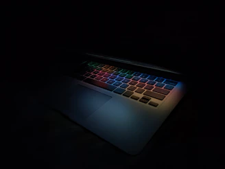 Close-up of a high-performance gaming laptop with colorful backlit keys glowing in a dark room.