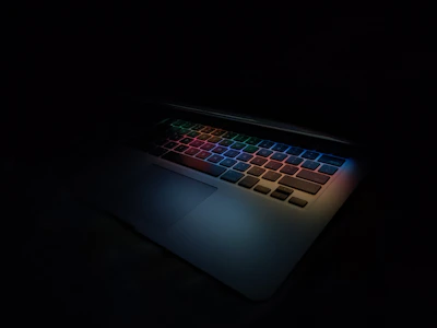 Close-up of a high-performance gaming laptop with colorful backlit keys glowing in a dark room.