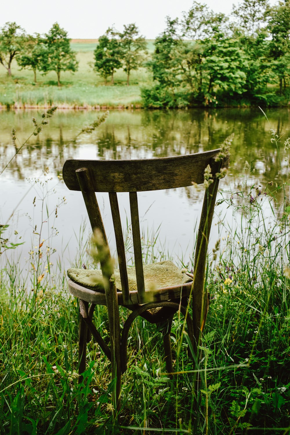 brown wooden chair on green grass near lake during daytime