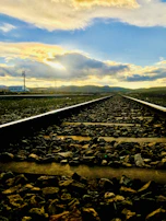 A modern railway track extending into the horizon with mountains in the distance during sunrise.