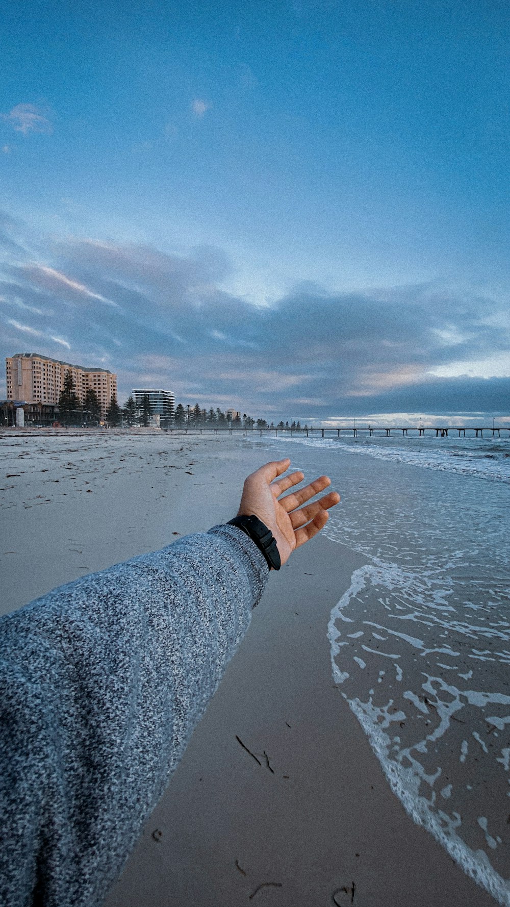 Person im grauen Langarmhemd, die tagsüber auf grauem Sand in der Nähe von Wasser steht