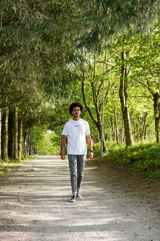 man in white crew neck t-shirt standing on pathway between trees during daytime in Sandnes Norway