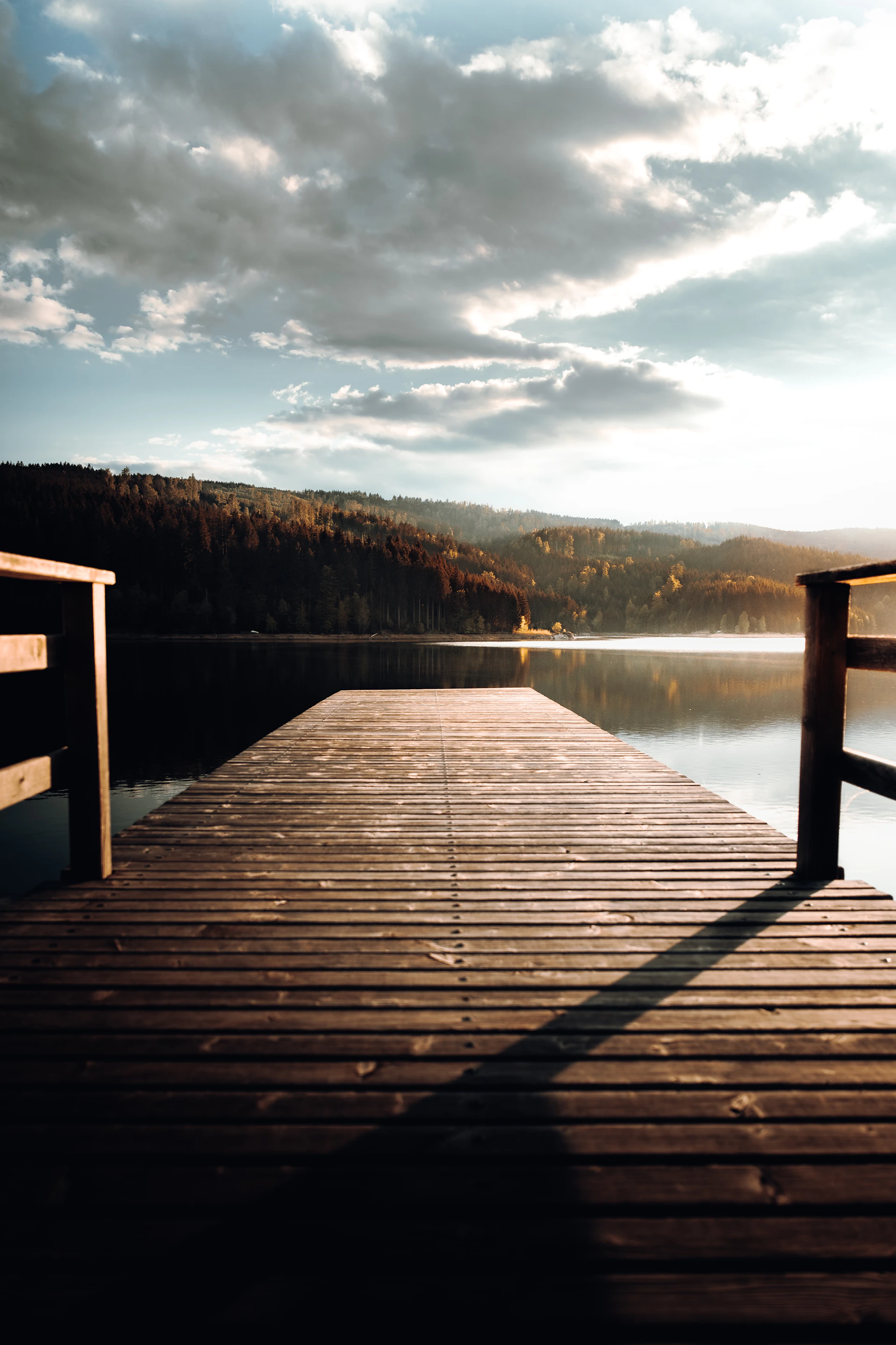 Close-up of a weathered wooden dock extending into a pristine lake, framed by lush evergreens under a soft twilight sky.