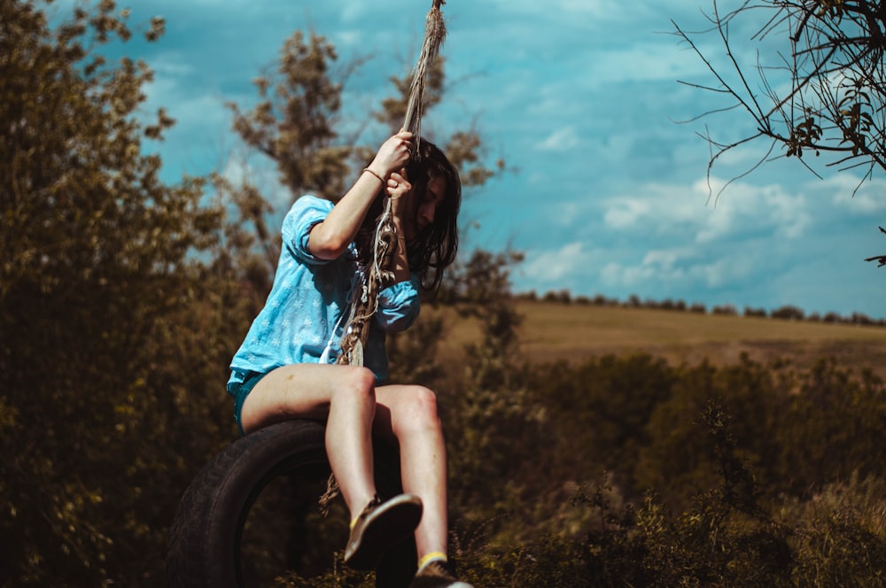 woman in blue and white plaid shirt sitting on tire swing during daytime