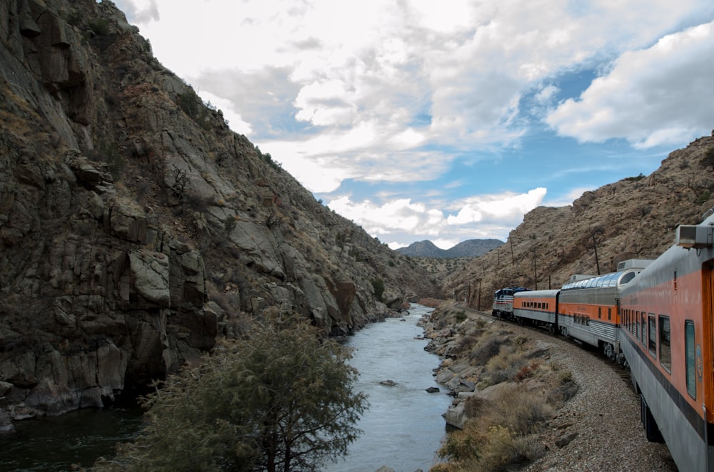 blue and white train on rail road near rocky mountain under white clouds and blue sky