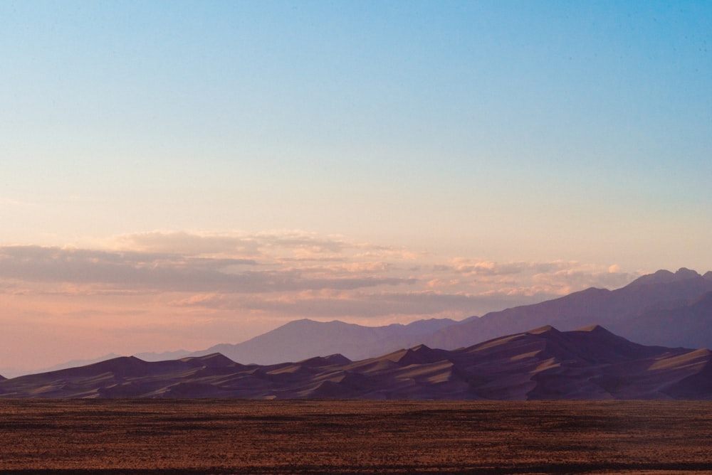 Campo marrón cerca de las montañas bajo el cielo azul durante el día