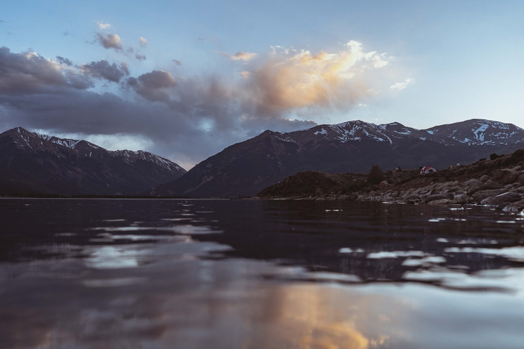 body of water near mountain under cloudy sky during daytime