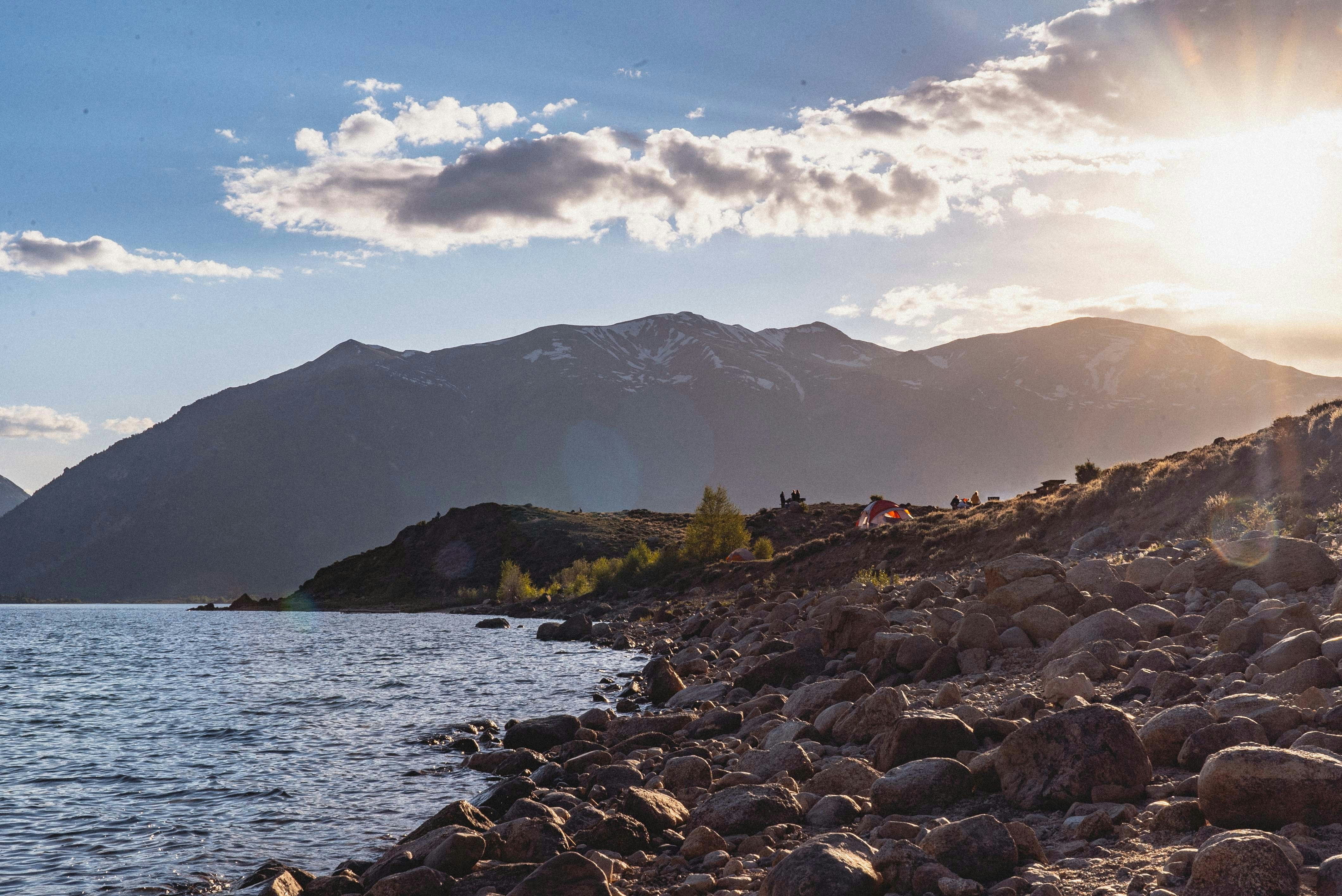 rocky shore with mountain in distance under blue sky with white clouds during daytime
