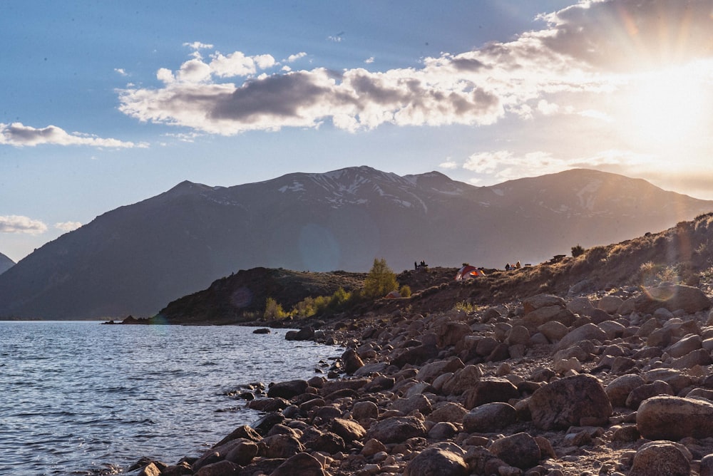 rocky shore with mountain in distance under blue sky with white clouds during daytime