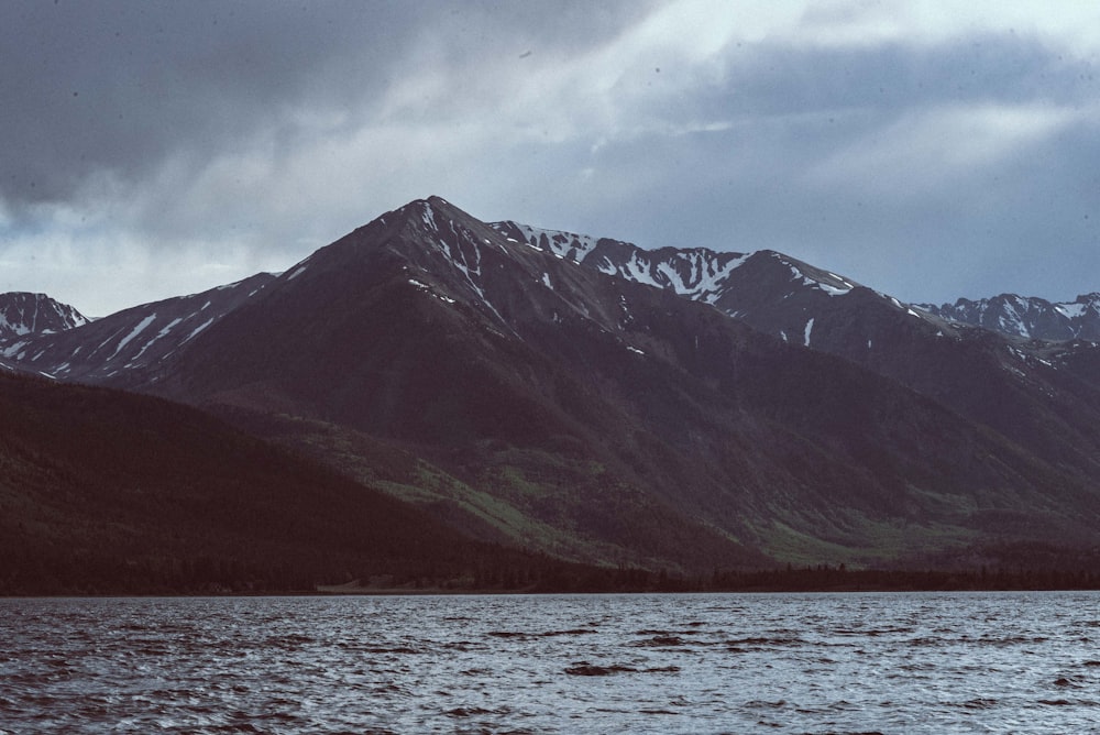 green and black mountain beside body of water under cloudy sky during daytime