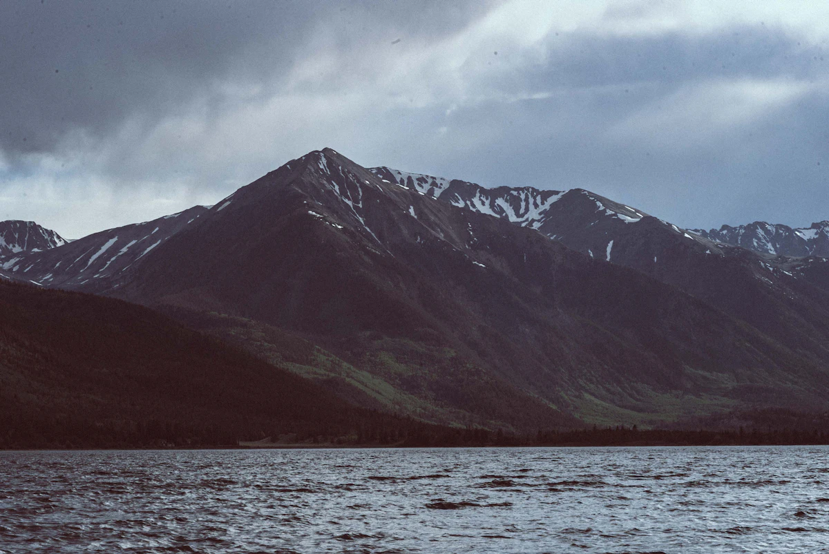 A dark mountain with patches of snow above choppy water at Twin Lakes, under storm clouds