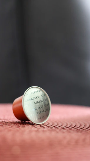 Close-up photo of a handcrafted coffee capsule brooch with a pearl centerpiece on a warm cream background.