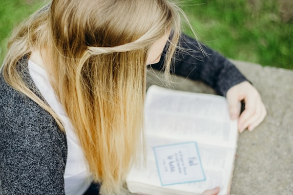 Fotografía de una joven leyendo un libro en un jardín.