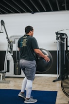 man in black t-shirt and blue denim jeans holding black exercise ball