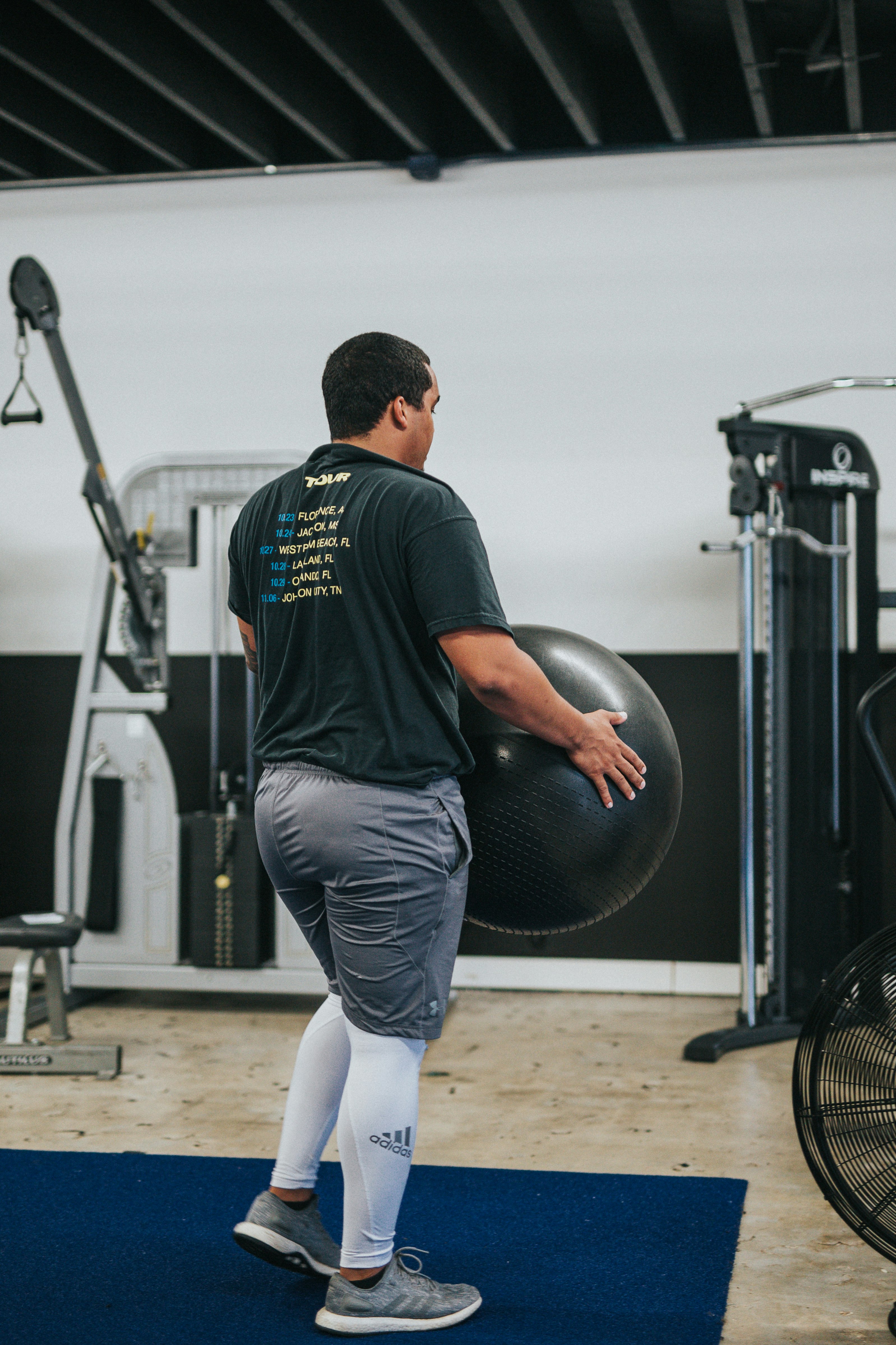 man in black t-shirt and blue denim jeans holding black exercise ball