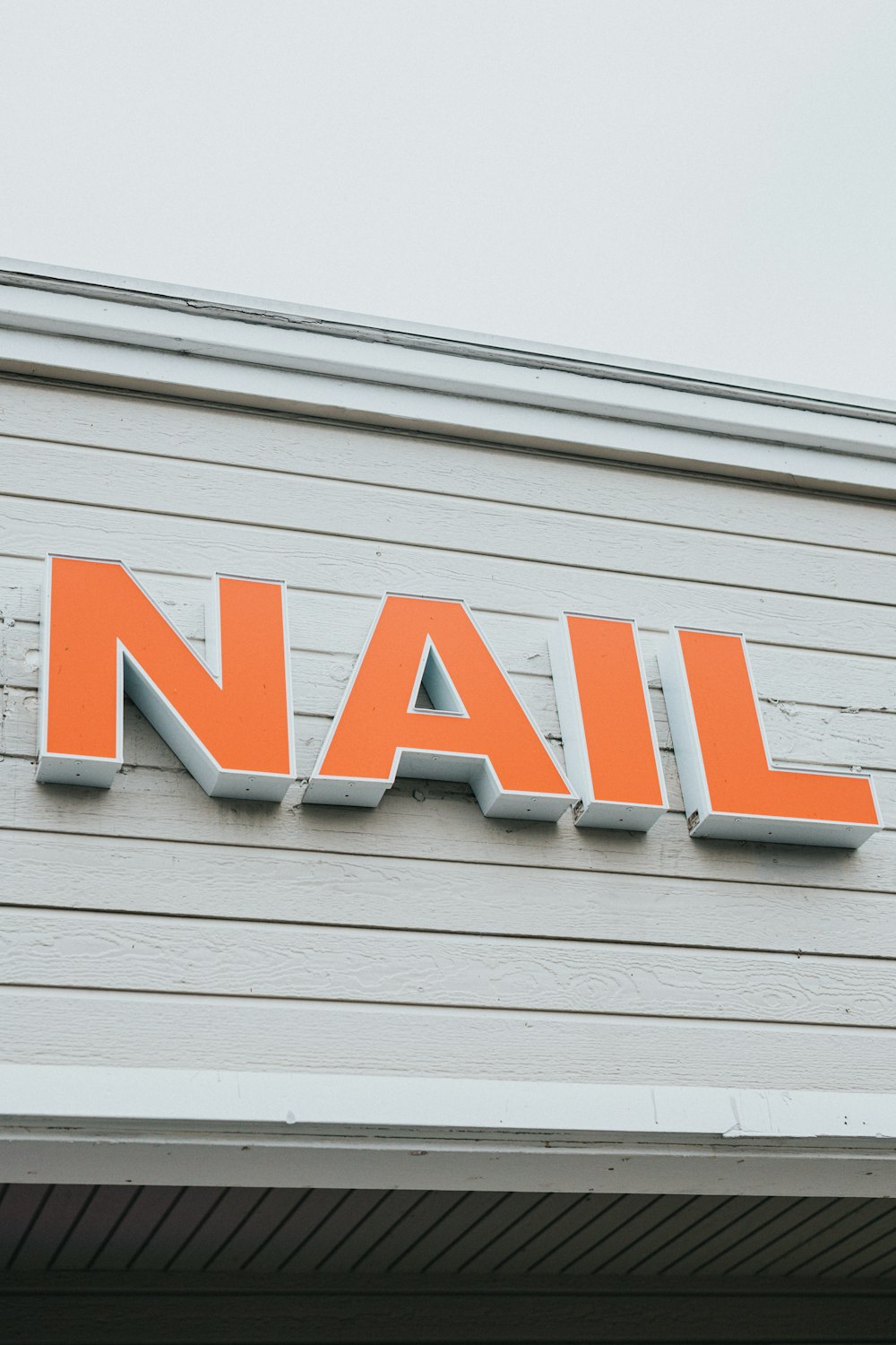 an orange nail sign on the side of a building