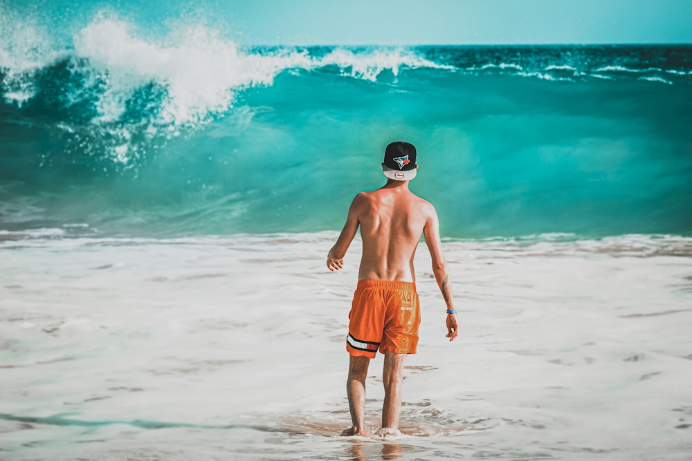 man in orange shorts standing on beach during daytime