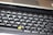 A close-up view of a computer keyboard, featuring a standard layout with English and additional non-Latin characters printed on the keys. The keys are mostly black with white and grey lettering, except for a few keys with orange symbols. The image is slightly out of focus, emphasizing a casual, everyday use context.