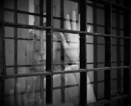 A tender moment of a hand reaching through a detention center window, fingers almost touching on either side.