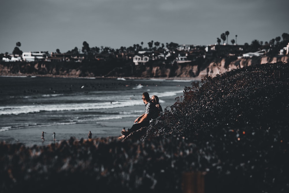 man in orange shirt and black shorts sitting on rock near body of water during daytime