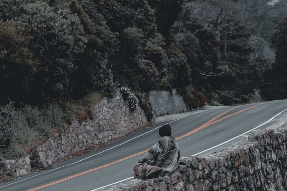 man in gray jacket sitting on gray asphalt road during daytime