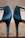 A close-up view of a pair of elegant, shiny high-heeled shoes with ankle straps. The shoes are positioned side by side with their heels and back sections prominently displayed. The background is blurred, which makes the shoes the central focus.