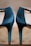 A close-up view of a pair of elegant, shiny high-heeled shoes with ankle straps. The shoes are positioned side by side with their heels and back sections prominently displayed. The background is blurred, which makes the shoes the central focus.
