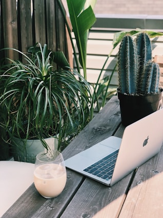 A relaxed freelancer working on a laptop at a cozy outdoor cafe with tropical plants around.