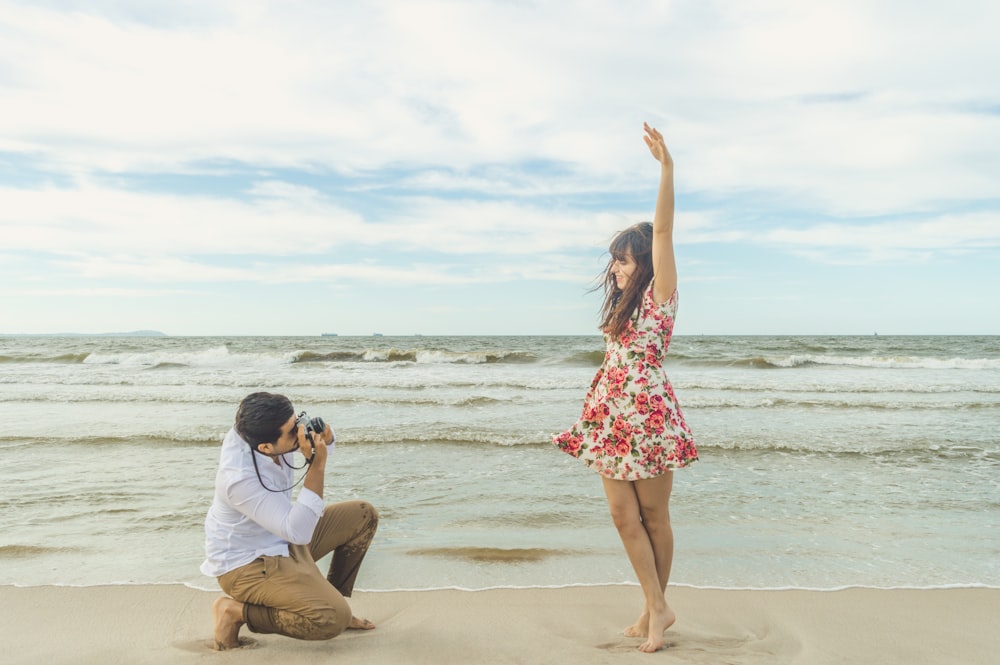 woman in white long sleeve shirt and red floral skirt standing on beach shore during daytime