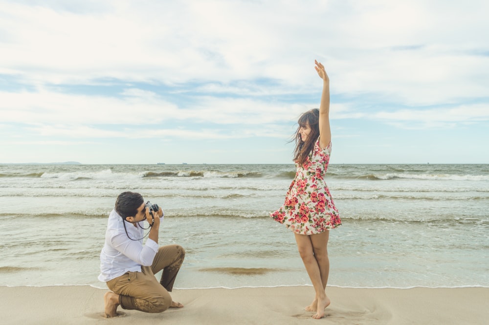 Femme en chemise blanche à manches longues et jupe à fleurs rouge debout sur le rivage de la plage pendant la journée