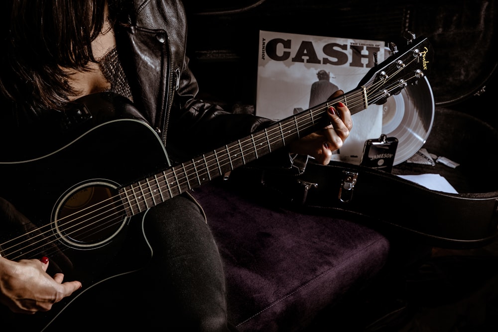 man in black leather jacket playing acoustic guitar