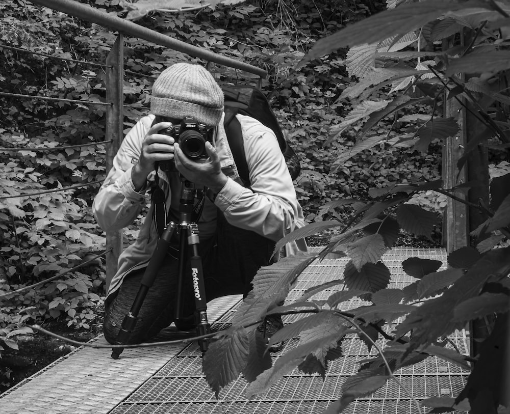 Foto en escala de grises de un hombre sosteniendo una cámara DSLR