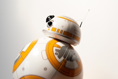 A spherical robot with a white body, orange circular patterns, and a dome-shaped head. The robot has a small antenna and black eye-like features on its head.