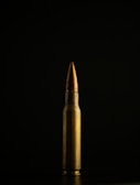 Close-up of a shiny copper bullet reflecting light on a dark background.
