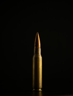 Close-up of a shiny copper bullet reflecting light on a dark background.