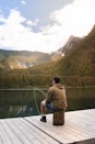 man in brown t-shirt and blue shorts standing on dock looking at lake during daytime