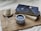 A cozy setting featuring a cup of coffee in a polka dot mug, placed next to two books with a celestial-themed cover on a wooden board. A white candle on a wooden coaster and delicate white flowers add to the tranquil ambiance.
