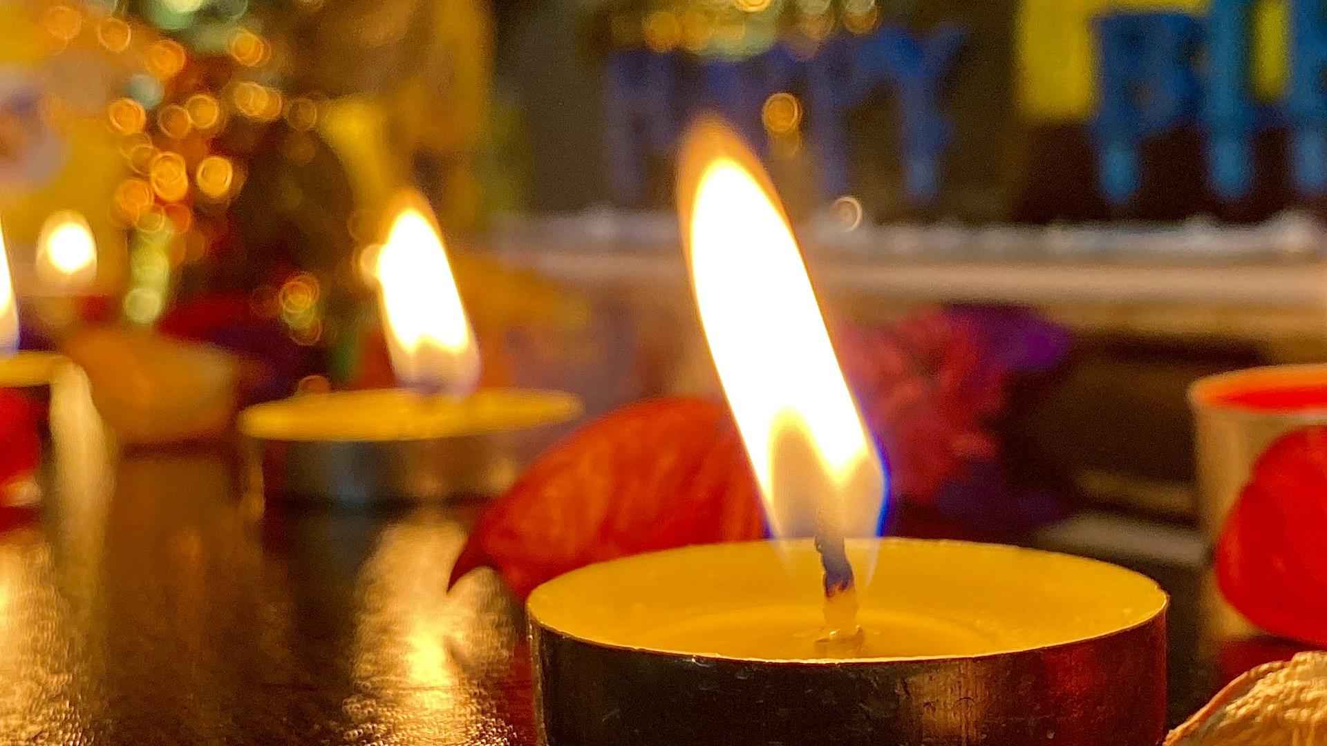 A collection of handcrafted tea lights flickering gently on a wooden tray, with subtle hints of Indian celebration colors in the background.