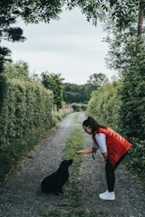 woman in orange long sleeve shirt and black pants holding black short coated dog