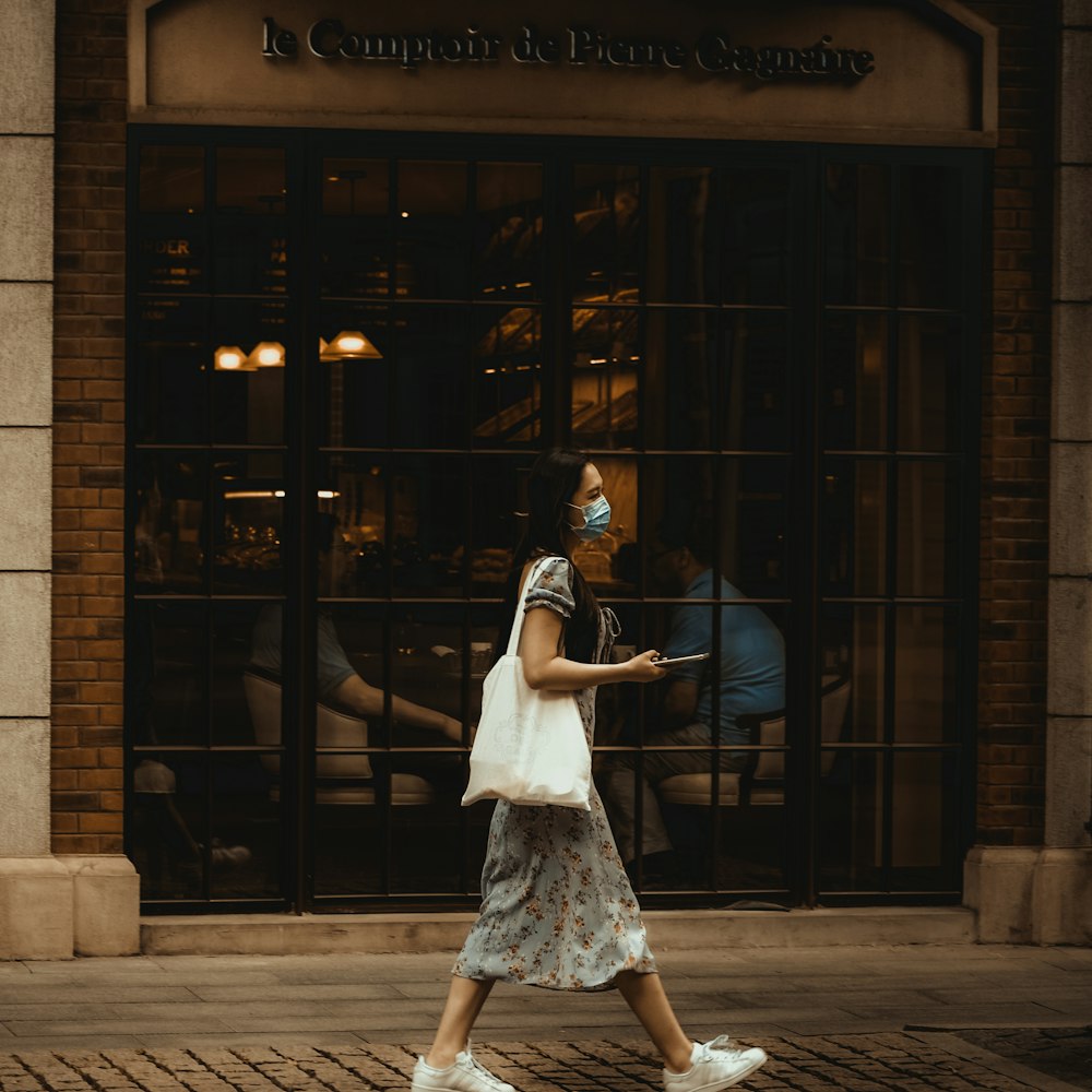 Femme en robe blanche debout près d’un bâtiment brun pendant la journée