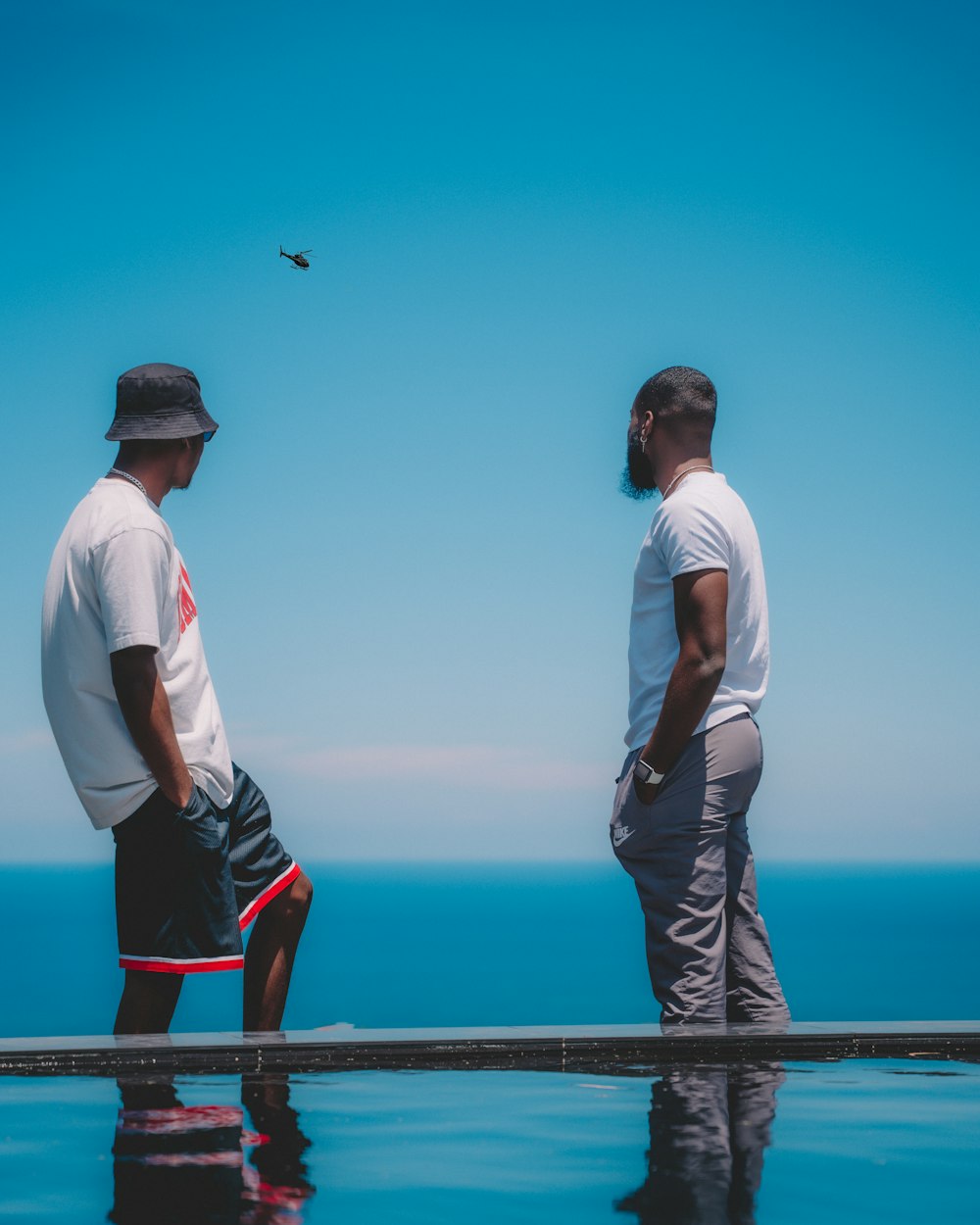 man in white shirt and brown pants standing on a dock looking at the sea during