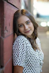woman in white and black polka dot shirt leaning on red wall