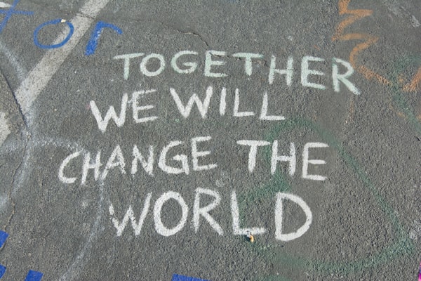 the words "together we will change the world" drawn in white chalk on asphalt