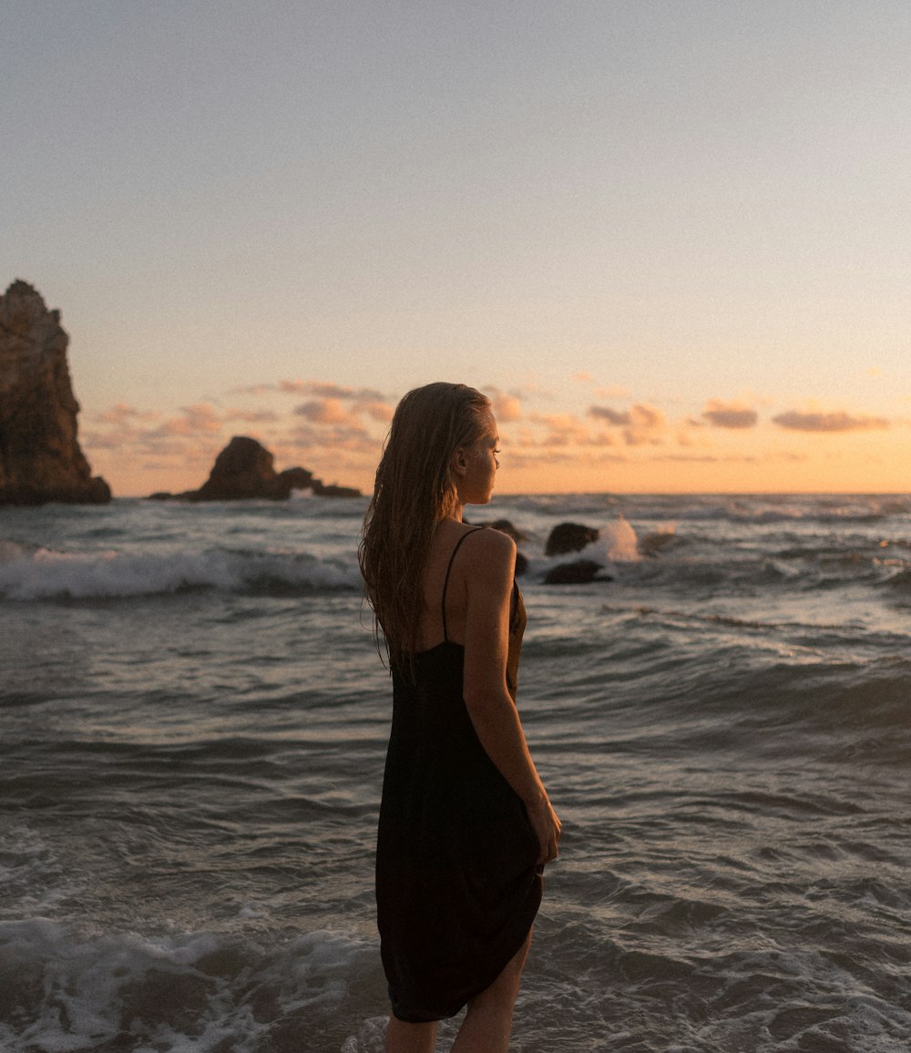 femme en robe noire debout sur le bord de mer pendant la journée