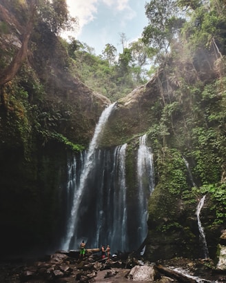 person in red jacket standing on rock near waterfalls during daytime