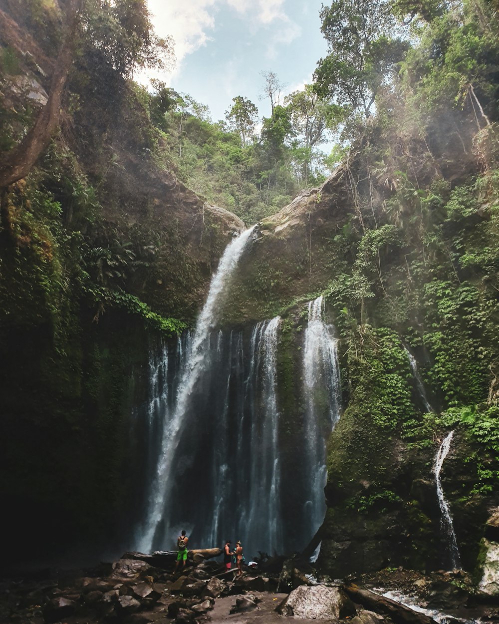 person in red jacket standing on rock near waterfalls during daytime